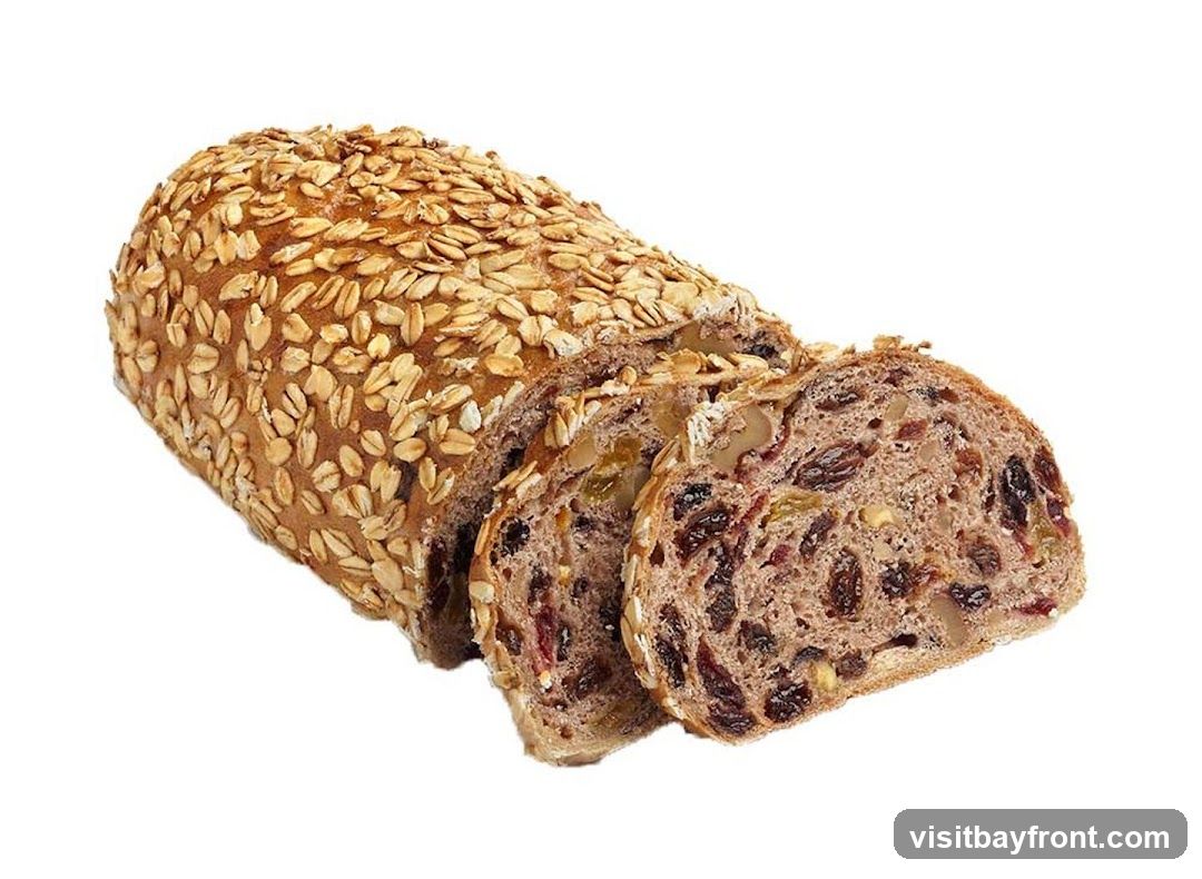 Four types of baked goods on a white background: a long loaf with dark speckles, a small oval bun with sesame seeds on top, a round golden-brown bun, and a flat circular bread with raisins. All appear freshly baked with shiny crusts.