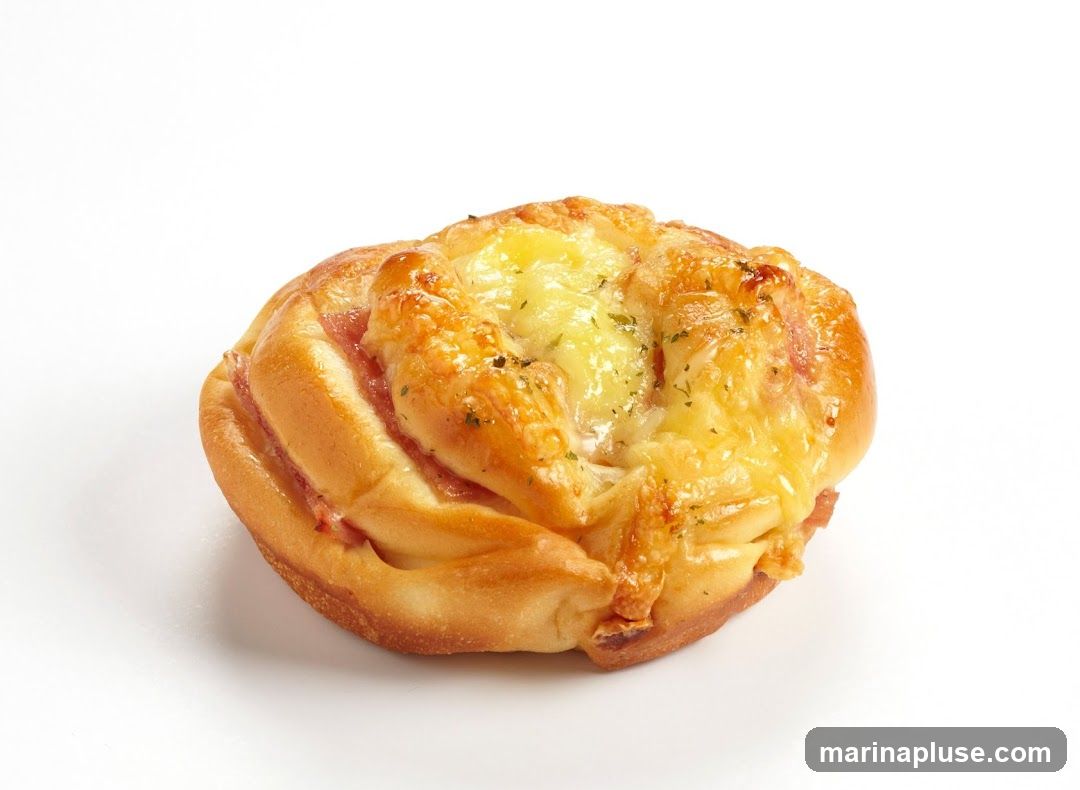 A single baked pastry with golden-brown crust, layered with ham and melted cheese, garnished with herbs, photographed against a plain white background.