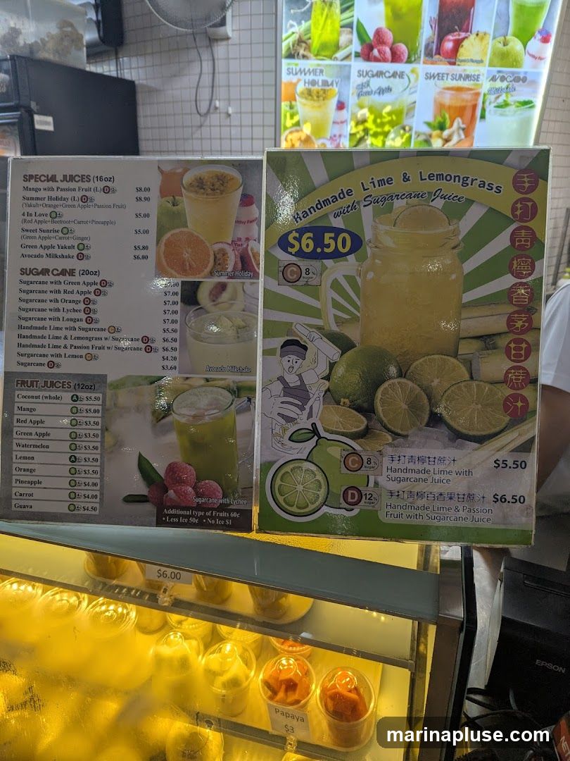 A menu board displaying various juices and milkshakes, with a featured item of "Handmade Lime & Lemongrass with Sugarcane Juice". Below the menu board, a display case shows cups of fruit, including papaya.