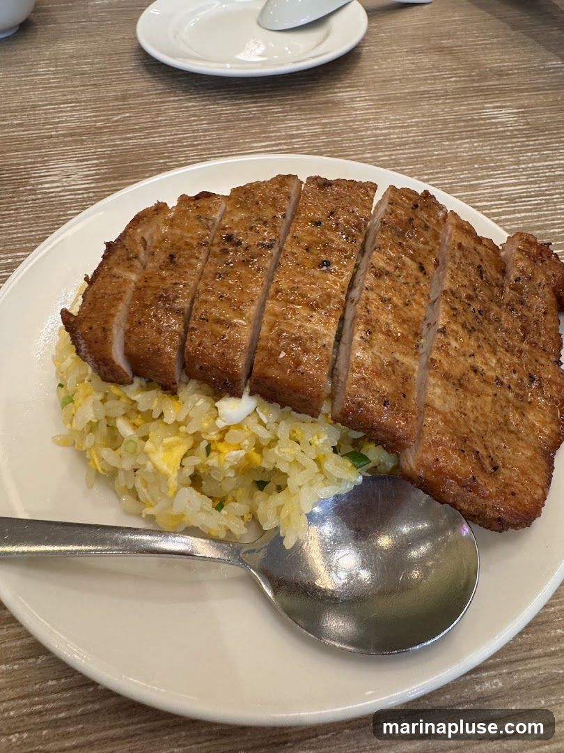 A close-up shot of a plate of fried rice topped with sliced grilled pork chops. A spoon rests on the side of the plate.
