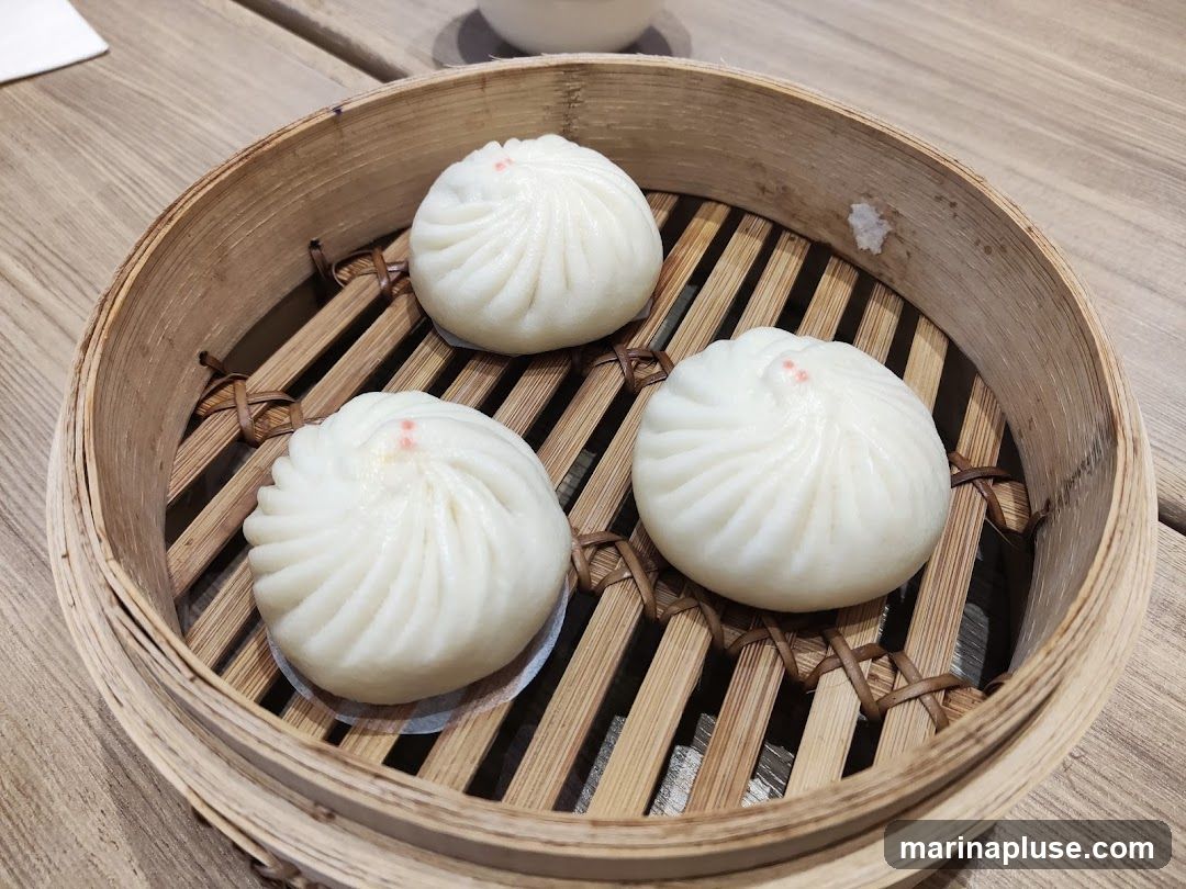 Three steamed buns with a swirl pattern and a small red dot on top, served in a bamboo steamer basket on a wooden table.