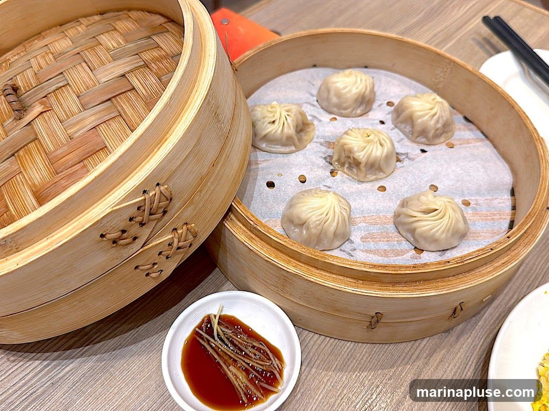 A close-up shot of steamed dumplings in bamboo steamers, served with a side of dipping sauce and shredded ginger.
