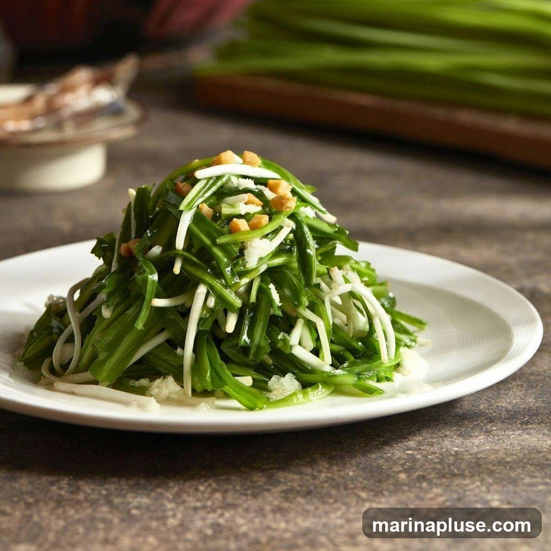A close-up shot of a plate of stir-fried green vegetables, possibly garlic scapes or chives, mixed with white shredded ingredients and topped with small croutons. The dish is served on a white plate and is presented on a textured, dark surface. In the background, more green vegetables are visible on a wooden board, along with a blurred bowl.