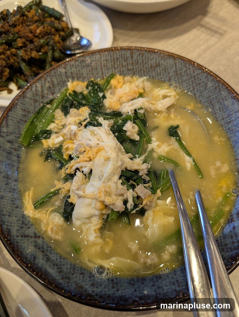 A close-up shot of a bowl of soup with spinach and scrambled egg. In the background, a dish of green beans is visible.