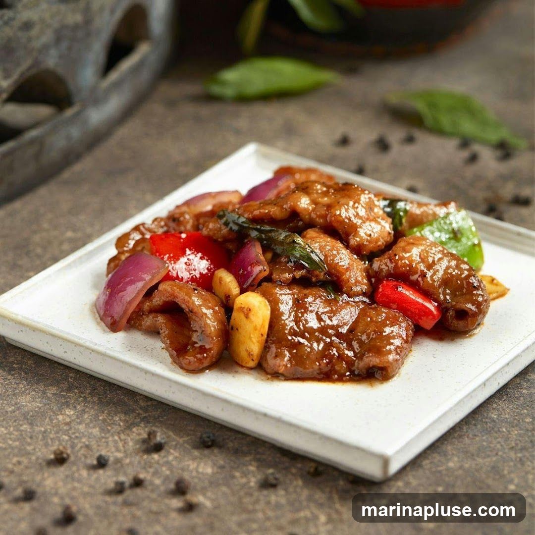 A close-up shot of a plate of stir-fried beef with red onions, red and green bell peppers, and what appear to be water chestnuts. The dish is coated in a glossy brown sauce and is presented on a white square plate. The background is a textured surface with scattered peppercorns and blurred greenery.