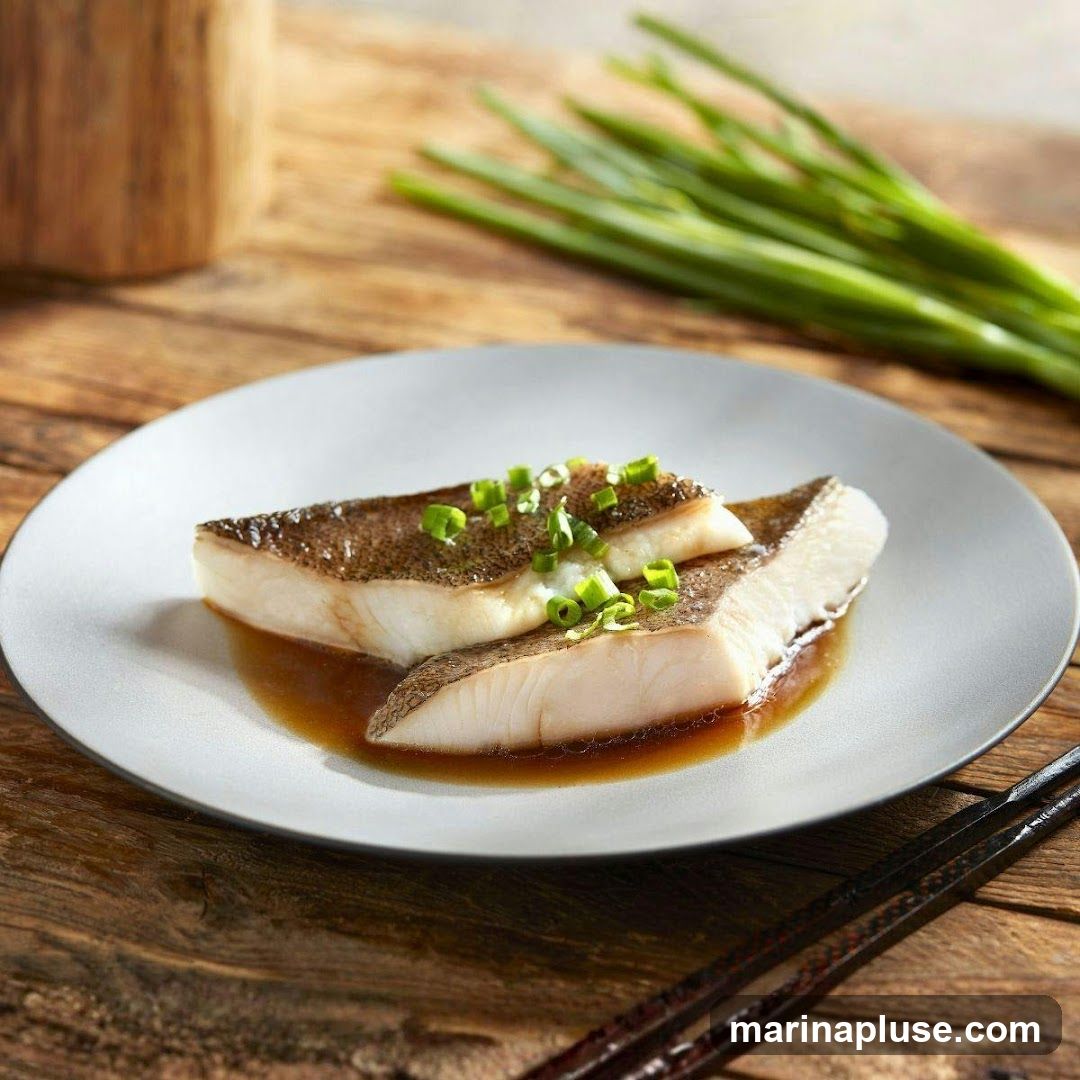 Two pieces of steamed fish fillets, garnished with chopped green onions, sit in a light brown sauce on a grey plate. The plate is placed on a rustic wooden surface. In the background, a wooden container and a bunch of green onions are visible. A pair of chopsticks rests on the right side of the plate.