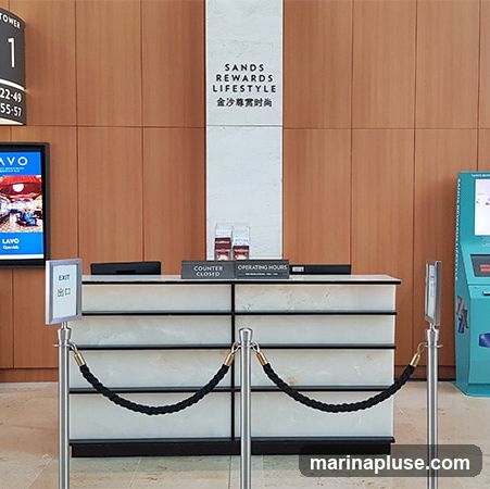 A counter with "Sands Rewards Lifestyle" signage above it. There are signs indicating "Counter Closed" and "Operating Hours". To the left, a digital display shows "LAVO" and an "EXIT" sign. To the right, a kiosk is visible.