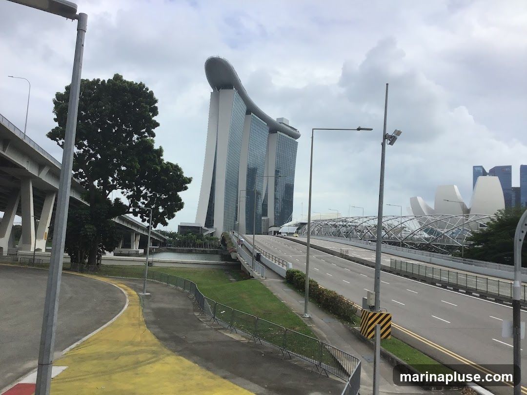 A view of the Marina Bay Sands hotel and the ArtScience Museum in Singapore, with a highway and pedestrian walkway in the foreground. The sky is overcast.