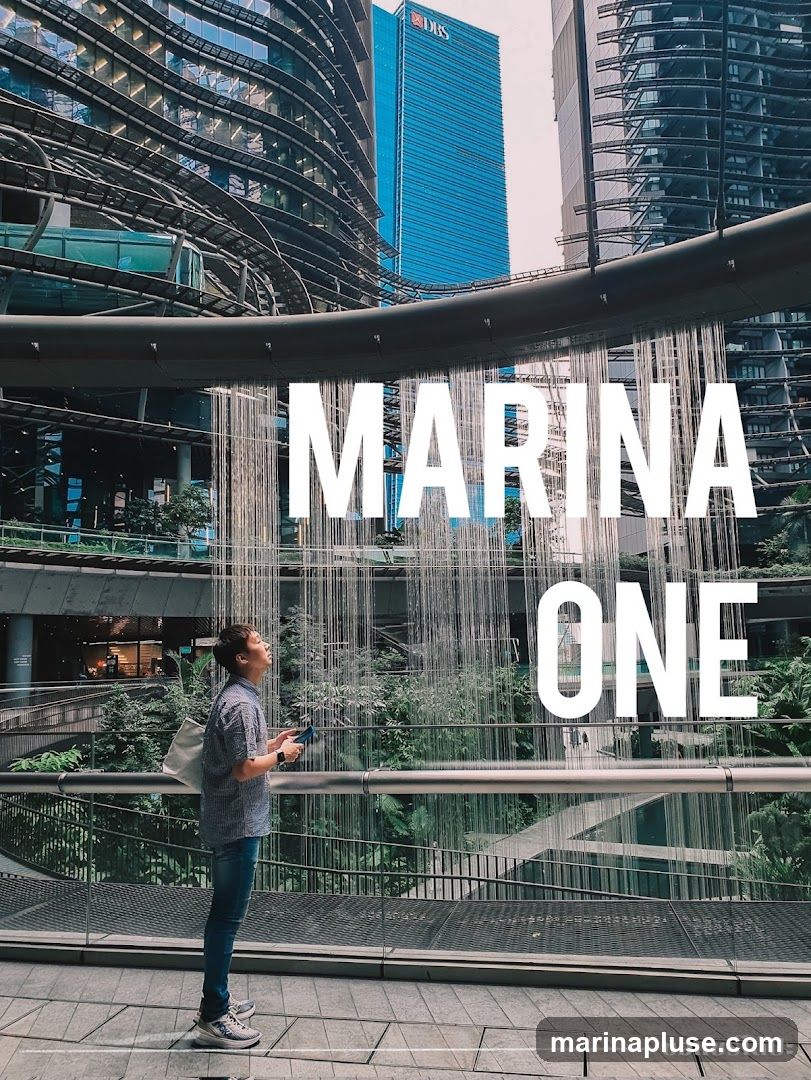 A person stands on a walkway looking up at a modern building with a waterfall feature. The words "MARINA ONE" are superimposed on the image.