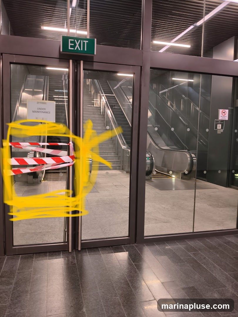 Glass doors with an "EXIT" sign above them. One door is covered with red and white caution tape and yellow scribbles. A sign on the door reads "UNDER MAINTENANCE". Escalators are visible behind the glass doors.
