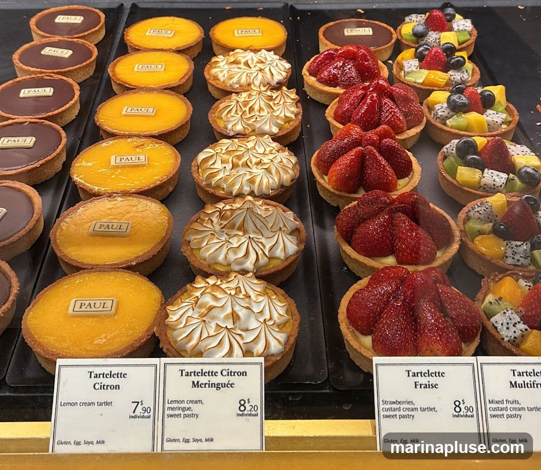 A display of various tarts, including chocolate, lemon, meringue, strawberry, and mixed fruit varieties. Each tart has a
