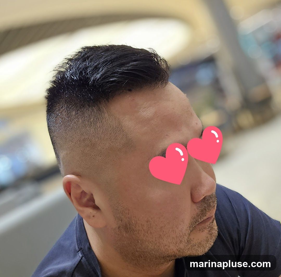A close-up profile shot of a man with a fade haircut. His eyes are covered with two pink heart stickers. The background is blurred, suggesting an indoor setting like a salon or public space.
