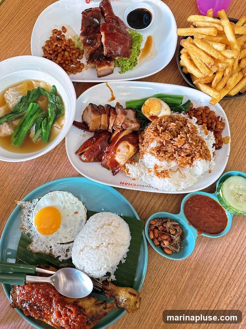 A variety of dishes are laid out on a wooden table. In the foreground, a plate features a fried egg, a mound of white rice, a piece of grilled chicken leg with sauce, and a small dish with anchovies, peanuts, and chili paste. To the right, a small dish contains cucumber slices and chili paste. In the background, another plate holds roasted meats, rice, a hard-boiled egg, and greens. A bowl of soup with wontons and greens is also visible, along with a pile of french fries. The plates have the text "HAWKER CHAN" printed on them.