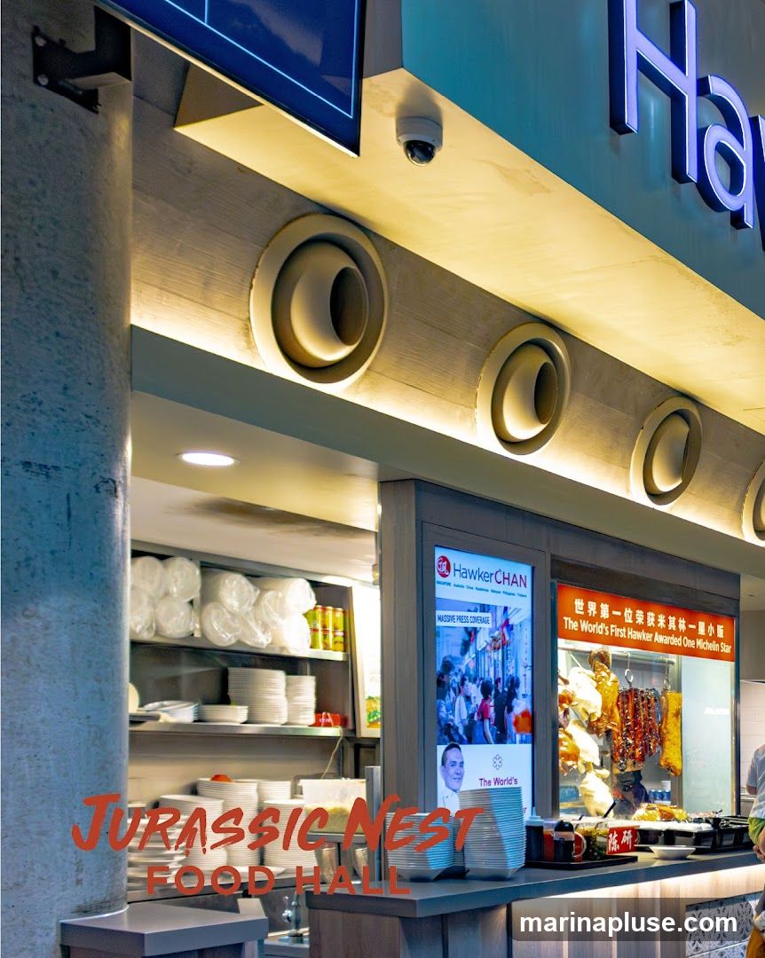A food stall in a food hall with a sign for Hawker Chan, which advertises "The World's First Hawker Awarded One Michelin Star" and "Massive Press Coverage." There are also hanging roasted meats and stacks of plates. The words "JURASSIC NEST FOOD HALL" are overlaid on the image.