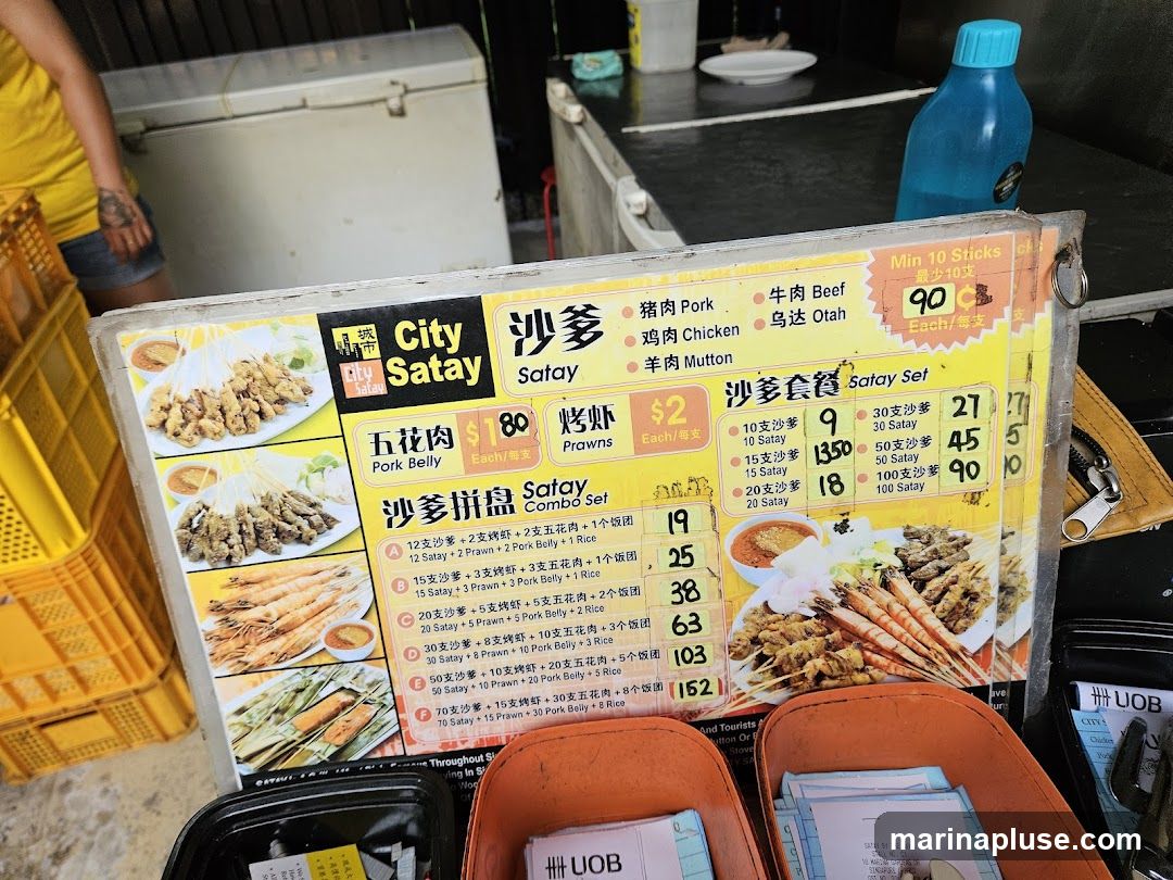 A menu board for City Satay offering various satay options, including pork belly, prawns, and combo sets. Prices are listed in SGD.