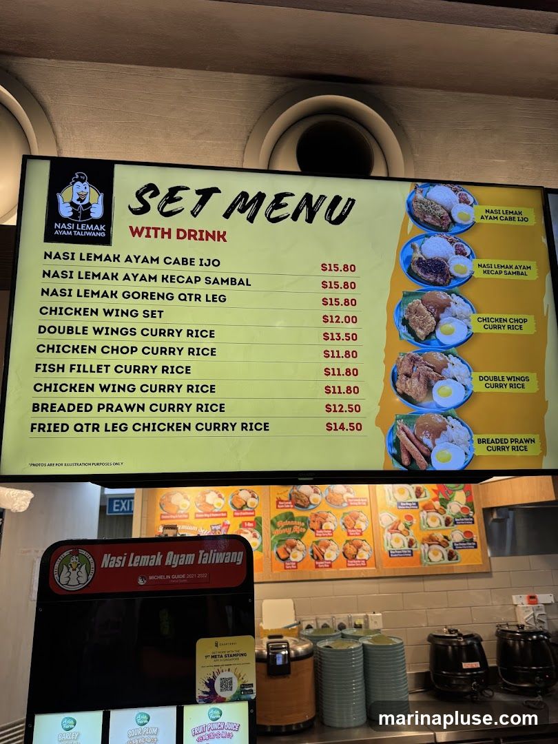 A digital menu board displays a list of Nasi Lemak set meals and curry rice dishes with prices. Images of some of the dishes are shown on the right side of the menu. Below the main menu, there is a sign for "Nasi Lemak Ayam Taliwang" and a list of drinks.