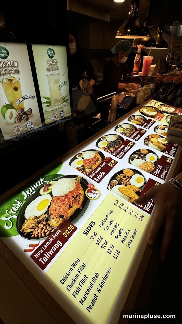 A brightly lit menu display featuring various Nasi Lemak dishes and sides. The menu shows images of the food items and their prices.