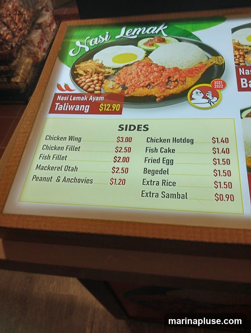 A menu board displaying Nasi Lemak Ayam Taliwang and various sides.