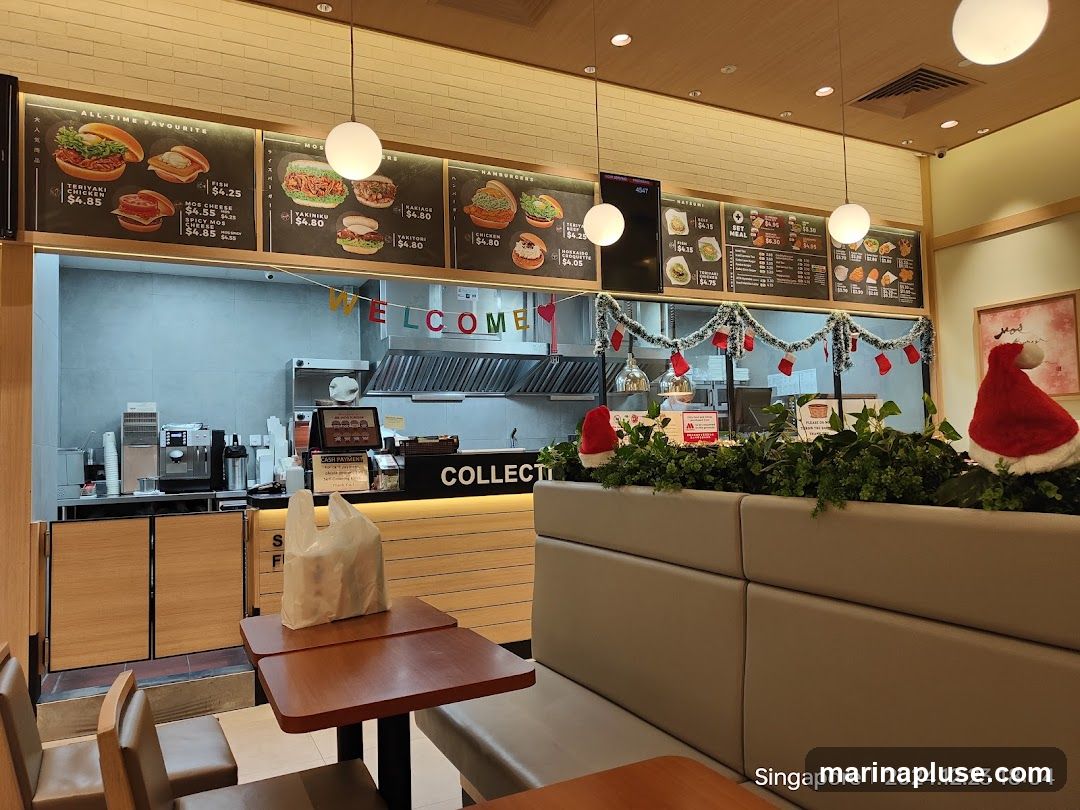 The image shows the interior of a restaurant with several menu boards displayed above the counter. The menus feature various food items like teriyaki chicken, fish, and hamburgers, with prices listed. A "WELCOME" banner hangs across the counter, and festive Christmas decorations, including Santa hats and garlands, are visible. The counter area has a "COLLECTION" sign, and seating areas with tables and chairs are in the foreground.