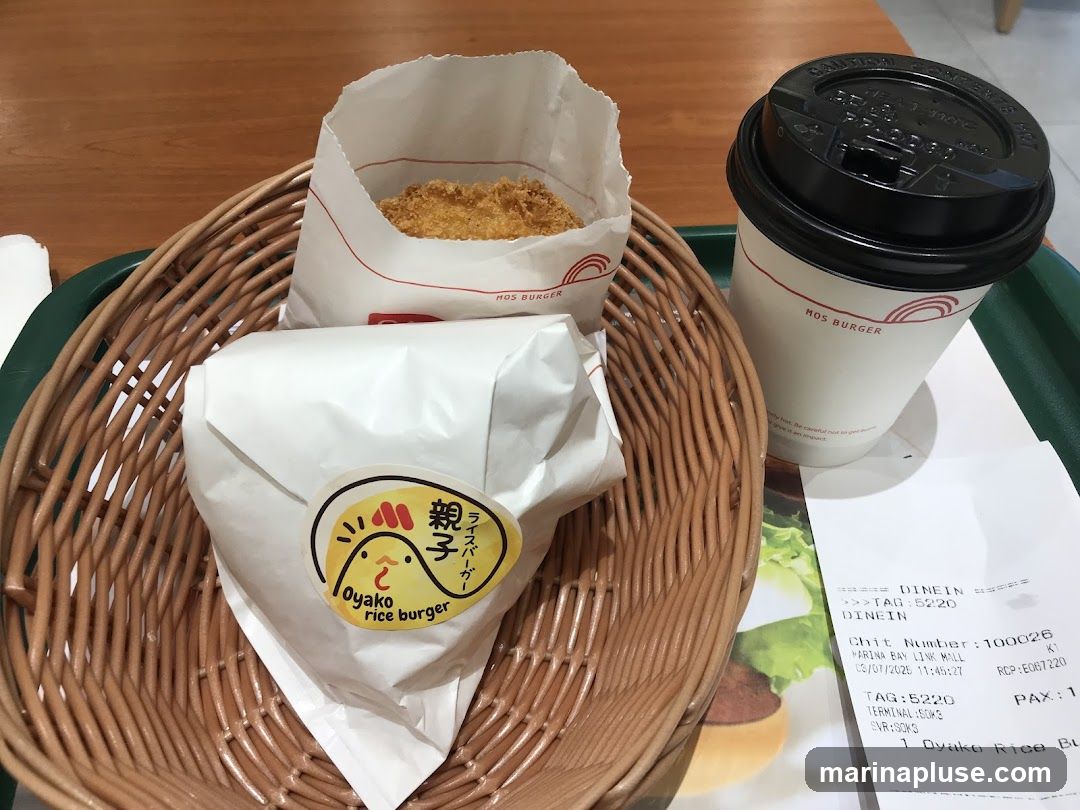 A woven basket holds a Mos Burger rice burger and a paper bag with a fried item. A cup of coffee with the Mos Burger logo is also on the tray, along with a receipt.
