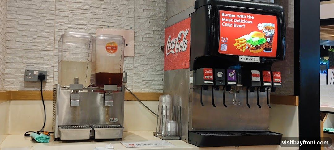 A selection of fried foods and Coca-Cola drinks from Mos Burger. The meal includes french fries, onion rings, chicken nuggets, and fried shrimp. Three glasses of Coca-Cola, labeled as 'Original Taste Less Sugar', are also visible. The Mos Burger logo is present in the upper right corner.