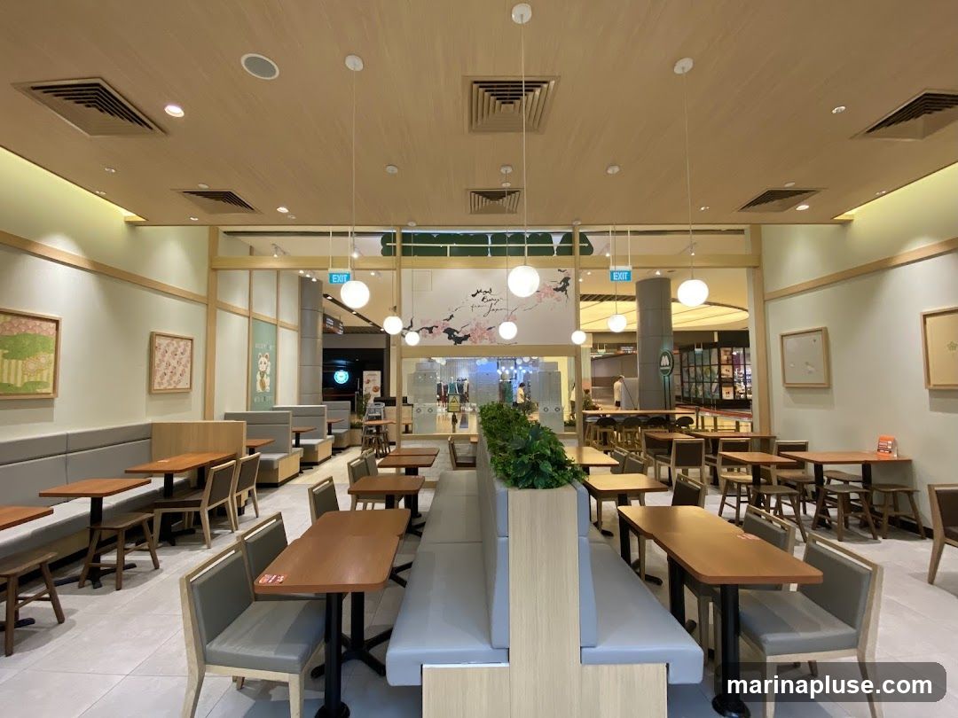The interior of a restaurant with wooden tables and chairs, booth seating, and decorative artwork on the walls. The space is well-lit with pendant lights and recessed lighting. An "EXIT" sign is visible in the background.