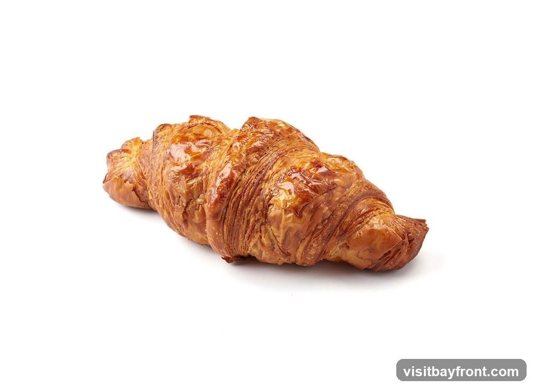 A single golden-brown croissant with a glossy surface, photographed against a plain white background.