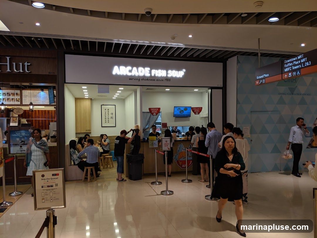 The exterior of a food stall called Arcade Fish Soup, with a sign above the counter. People are queuing and ordering food.