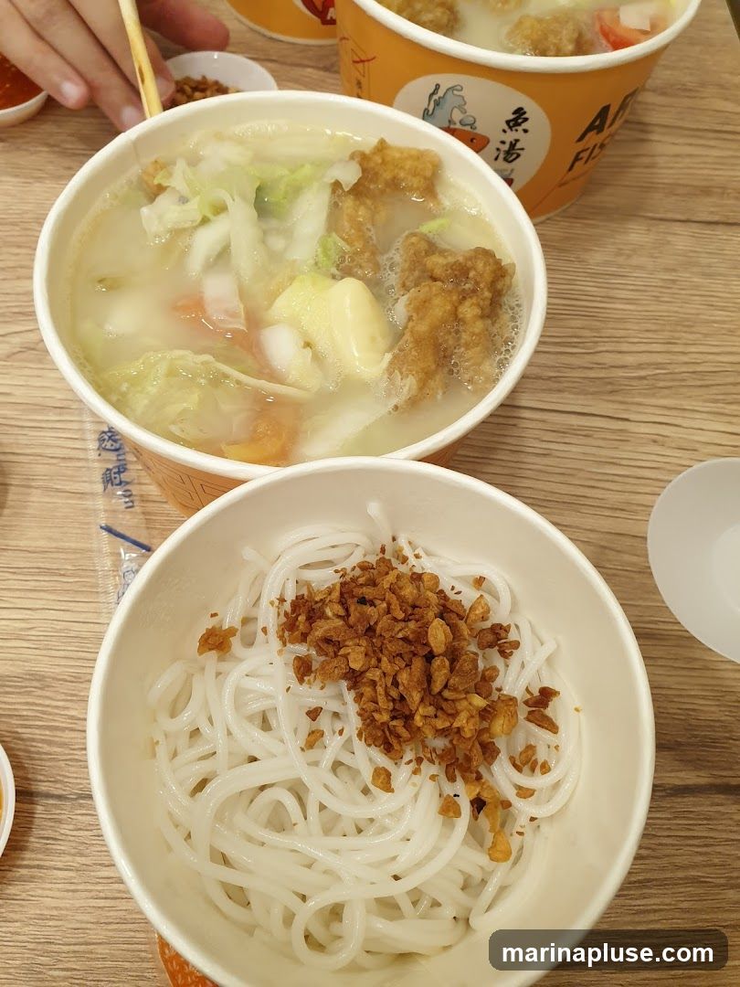 Two bowls of food are shown on a wooden table. The bowl in the foreground contains white noodles topped with fried garlic bits. The bowl in the background contains a soup with cabbage, fried fish pieces, and other vegetables. The bowls have orange branding with Chinese characters and the text "AR FISH".