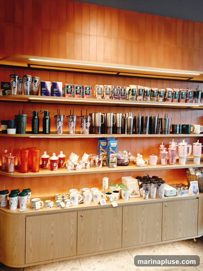 Shelves filled with various Starbucks merchandise, including tumblers, mugs, water bottles, and packaged coffee. The display features a prominent orange tiled wall and wooden cabinetry.