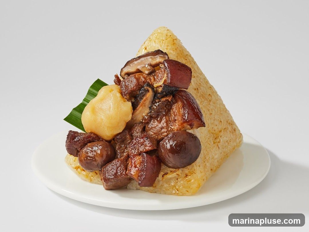 A triangular-shaped rice dish topped with braised meat, mushrooms, and a small round dumpling-like item, garnished with a green leaf, served on a white plate against a plain background.