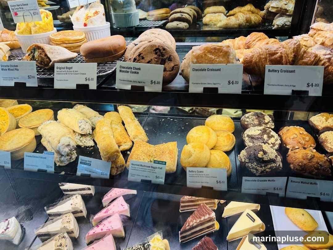 A display case filled with various baked goods including croissants, muffins, cookies, pastries, and cakes.