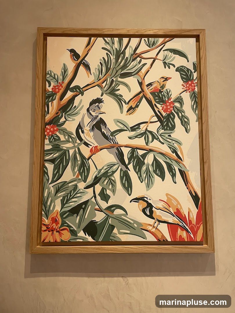A framed painting featuring a stylized depiction of birds perched on branches amidst lush foliage and red berries. The artwork has a light-colored background and is enclosed in a simple wooden frame.