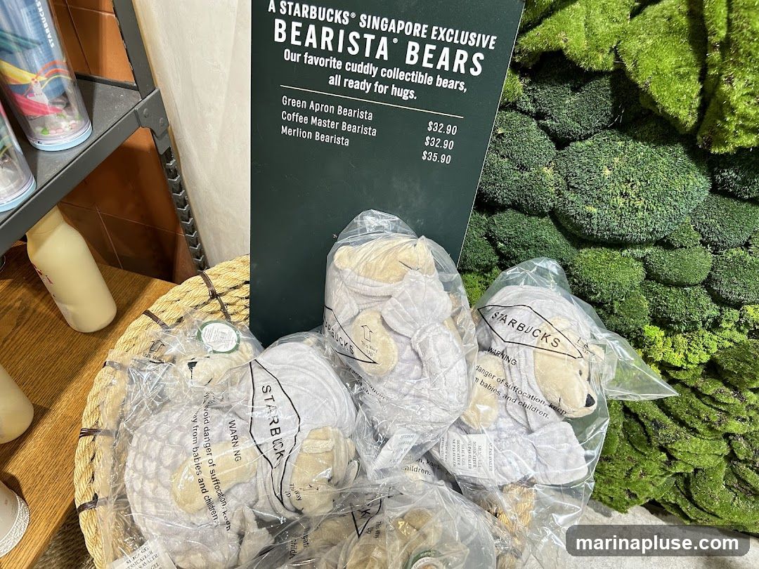 A display of Starbucks Bearista Bears, which are collectible bears exclusive to Singapore. The bears are packaged individually and are shown in a basket. A sign lists three types of bears: Green Apron Bearista, Coffee Master Bearista, and Merlion Bearista, with their prices. The background features a textured green wall resembling moss.