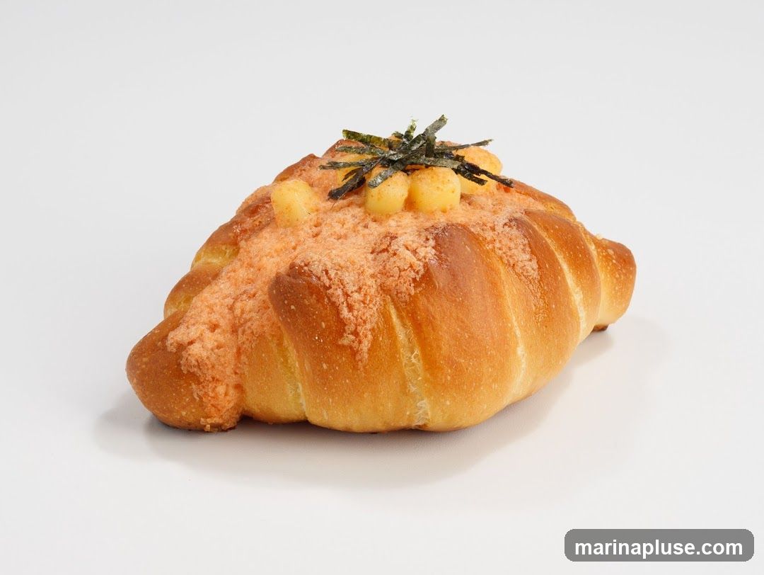 A single croissant-style pastry with a golden-brown crust, topped with orange-colored crumbs, small yellow spheres, and dark green seaweed flakes. The item is photographed against a plain white background.