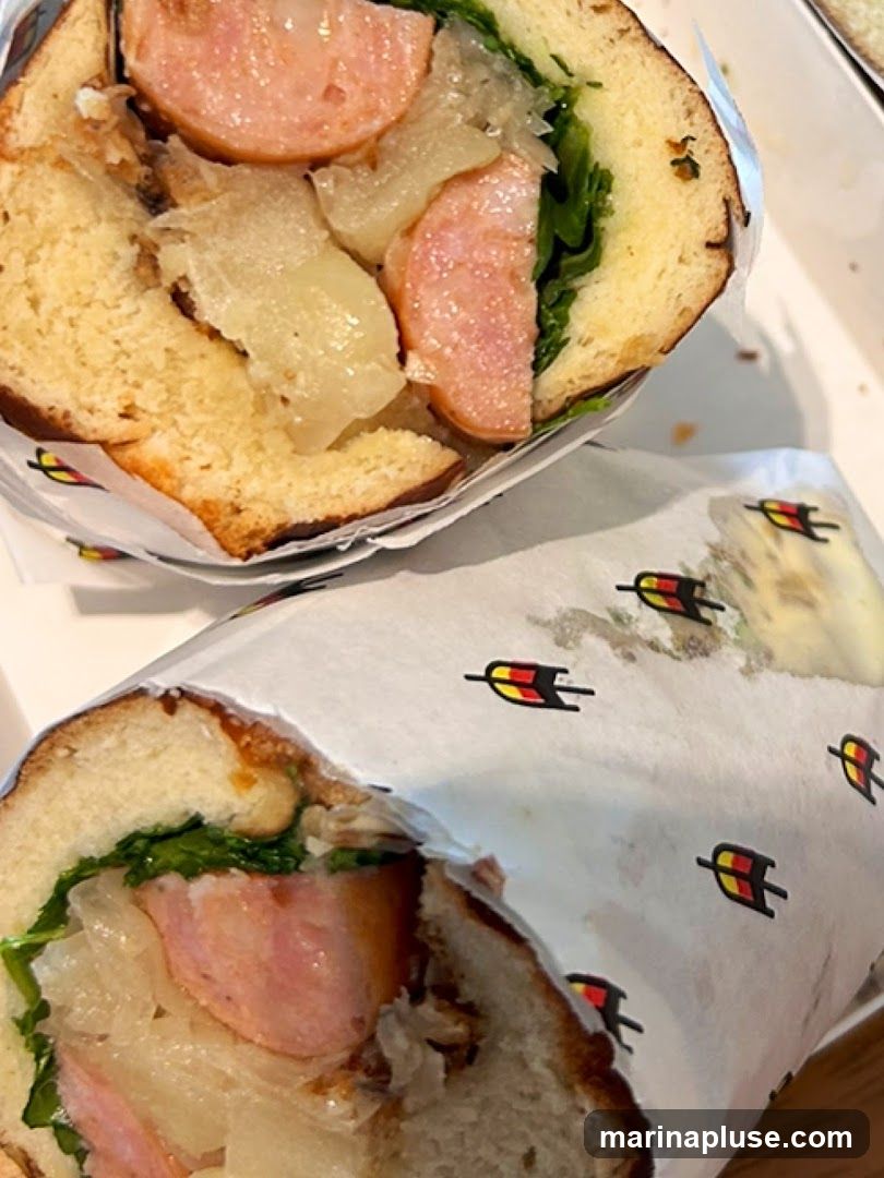 Two sandwiches are shown, wrapped in paper with a repeating logo. The sandwiches appear to be filled with sausage, greens, and some kind of relish or sauce.