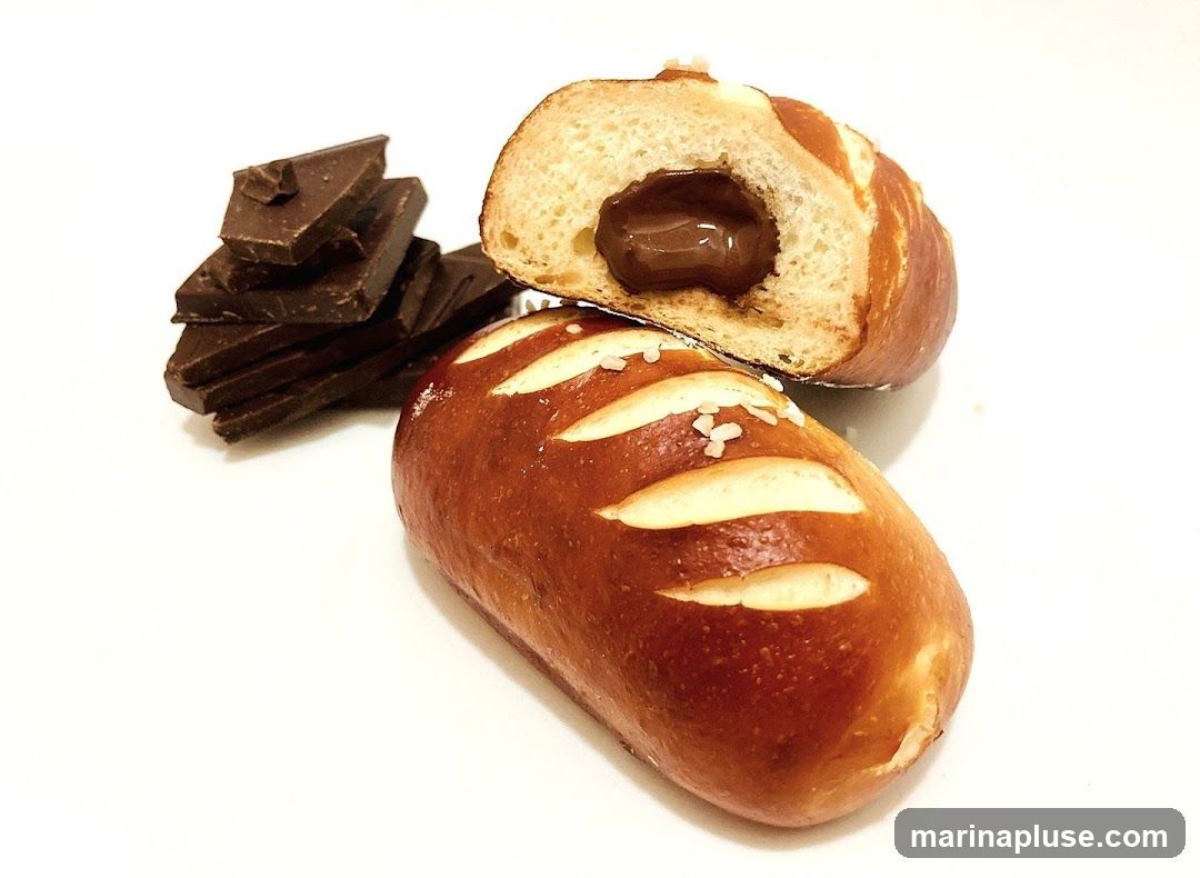 A close-up shot of a chocolate-filled pretzel bread, with one piece cut in half to reveal the rich chocolate filling. Beside the bread, a stack of dark chocolate squares is visible.