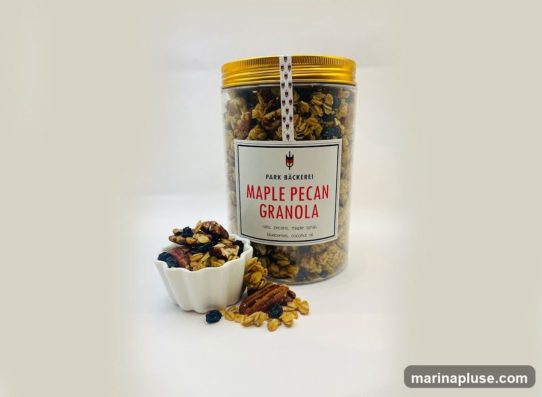 A clear plastic jar filled with maple pecan granola, with a small white bowl of granola in front of it. The label on the jar reads "PARK BÄCKEREI MAPLE PECAN GRANOLA" and lists ingredients as "oats, pecans, maple syrup, blueberries, coconut oil."