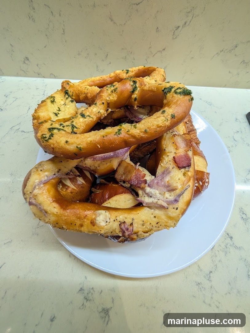 A white plate holds a pile of large, golden-brown pretzels. Some pretzels are topped with chopped green herbs, while others appear to be filled with red onion and possibly bacon bits. The pretzels are arranged in a rustic, appealing manner on the plate, which sits on a speckled countertop.