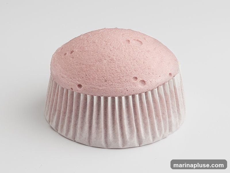 A single pink cupcake in a pleated paper liner, photographed against a plain white background.