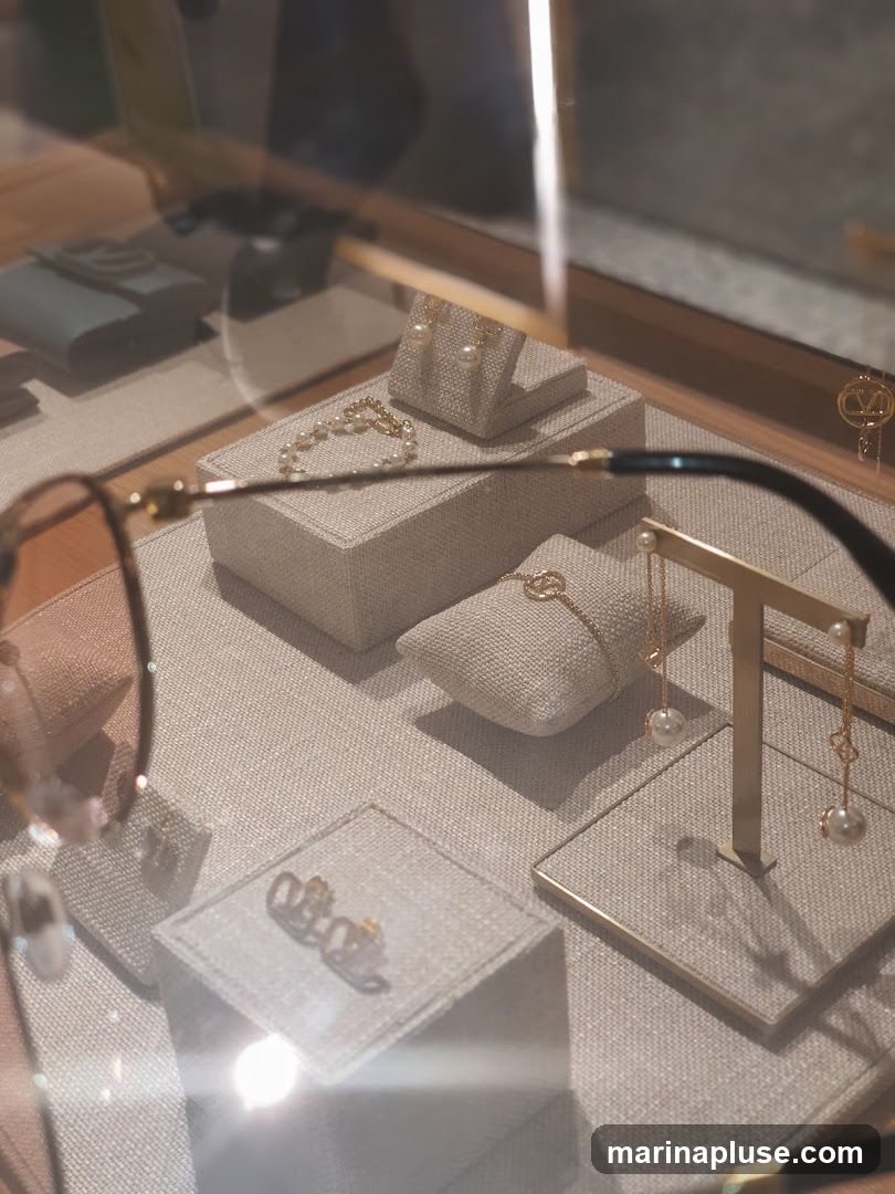 A close-up view of a jewelry display case, showcasing various pieces of pearl and gold jewelry, including earrings, bracelets, and rings. The items are arranged on textured stands within the case. A pair of glasses is partially visible in the foreground, suggesting the perspective of a customer.