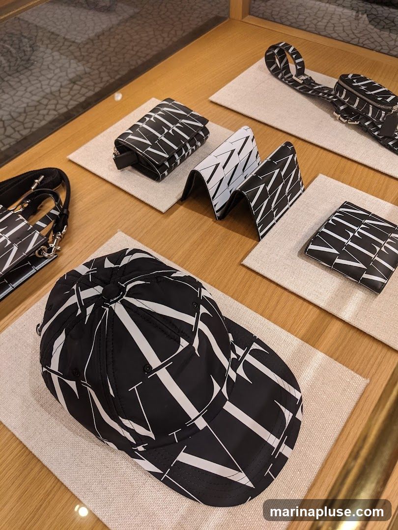 A display of luxury accessories, including a baseball cap, wallets, and a small bag, all featuring a repeating black and white logo pattern. The items are neatly arranged on a wooden surface with light-colored fabric mats.
