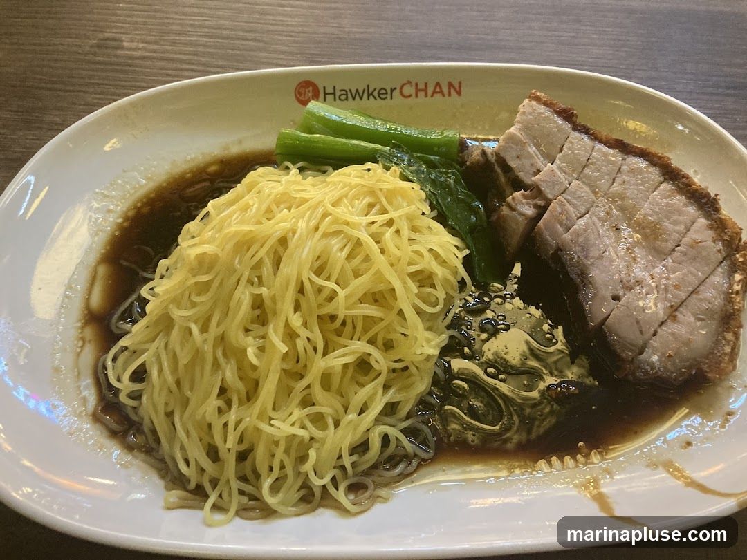 A plate of noodles with roasted pork and greens. The plate has the Hawker Chan logo.