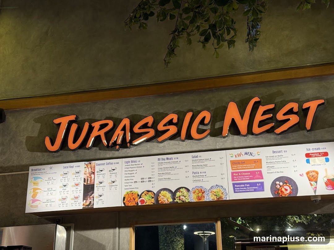 A menu board for Jurassic Nest restaurant, featuring breakfast, local kopi, gourmet coffee, light bites, all-day meals, salads, pasta, kids' meals, desserts, and ice cream.