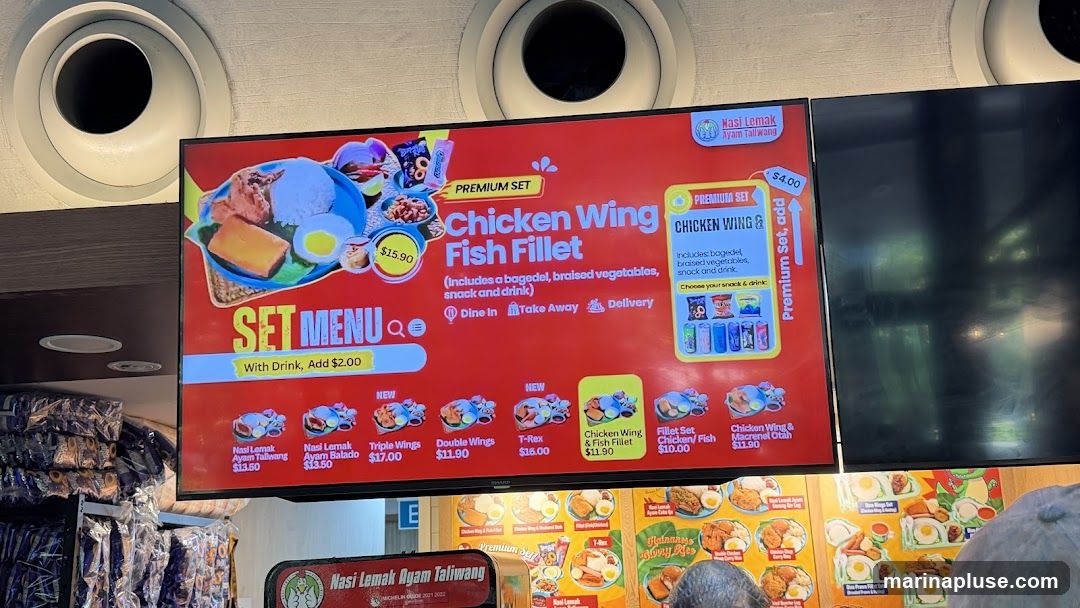 A digital menu board displays various set meals with images and prices. The main featured item is the 'Chicken Wing Fish Fillet' set for $15.90. Other options include Nasi Lemak Ayam Taliwang ($13.50), Nasi Lemak Ayam Balado ($13.50), Triple Wings ($17.00), Double Wings ($11.90), T-Rex ($16.00), Chicken Wing & Fish Fillet ($11.90), Fillet Set Chicken/Fish ($10.00), and Chicken Wing & Macrel Otah ($11.90). A premium set option for Chicken Wing & Fish Fillet is also shown for $4.00.