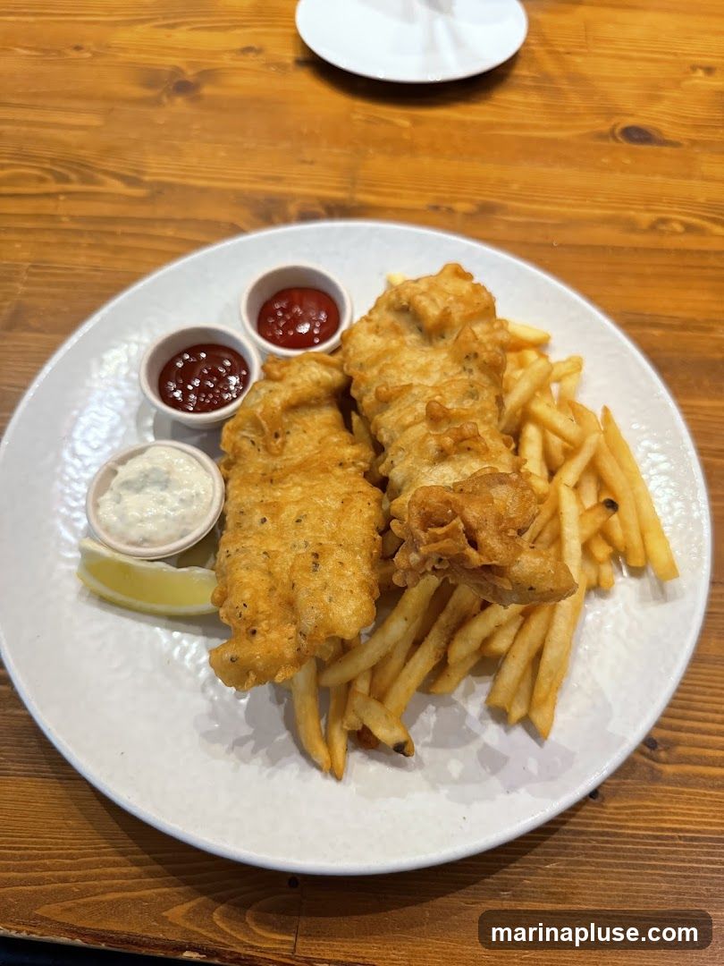 A plate of fish and chips served with tartar sauce, ketchup, and a lemon wedge on a wooden table.