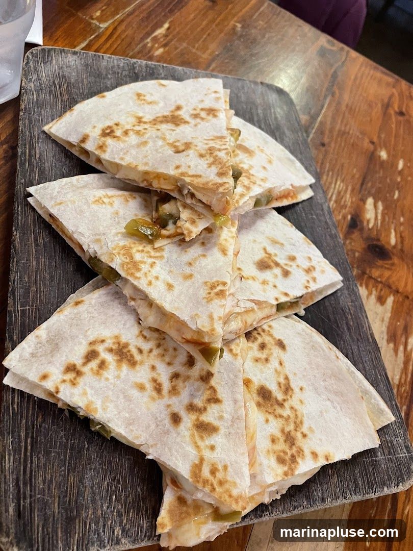 A close-up shot of quesadillas cut into wedges and served on a rustic wooden board. The quesadillas appear to be filled with cheese and green peppers.