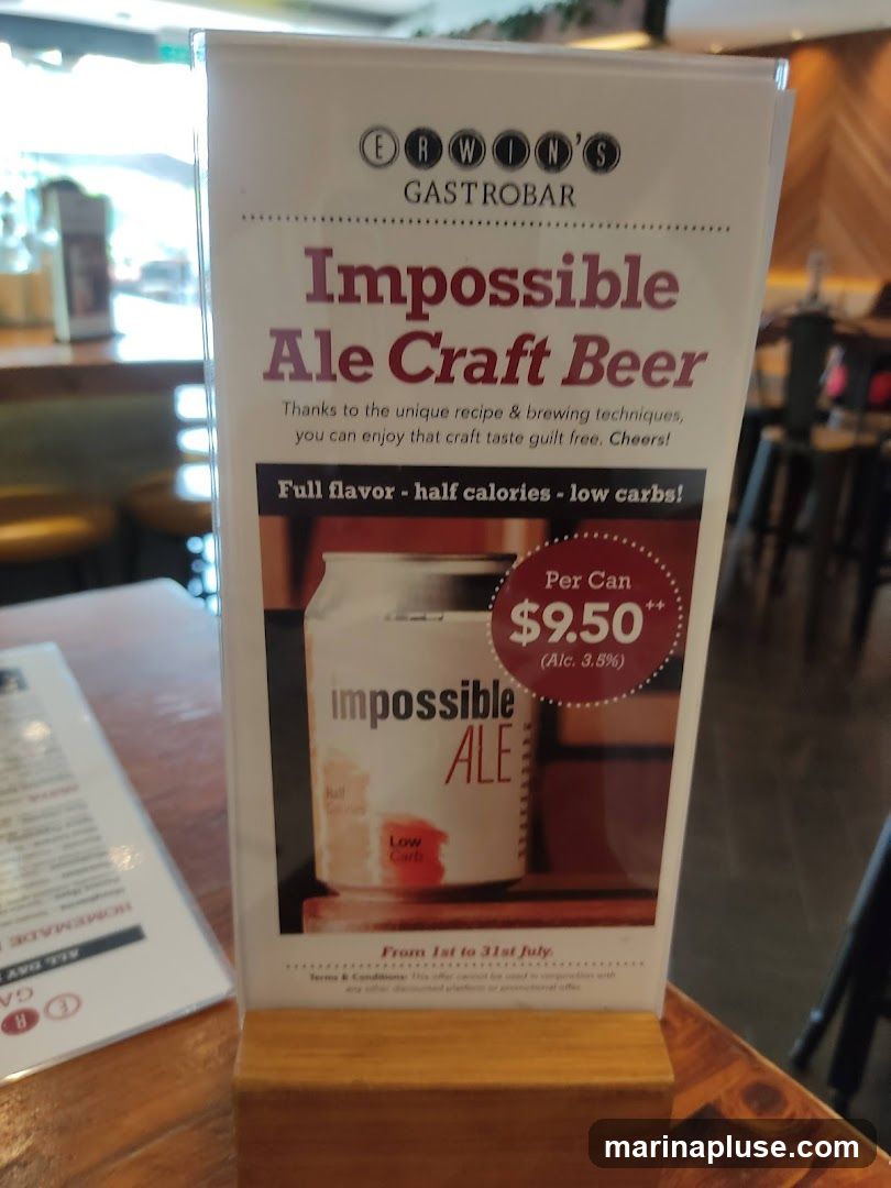 A promotional stand for Impossible Ale Craft Beer at Erwin's Gastrobar. The stand features an image of a can of Impossible Ale and highlights its low calorie and low carb content. It is priced at $9.50 per can and is available from July 1st to July 31st.