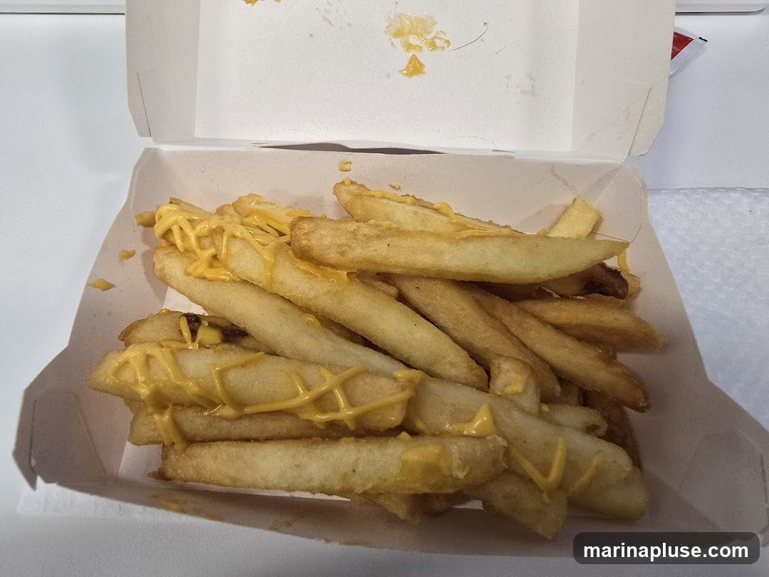 A white cardboard container filled with french fries topped with melted cheese sauce.