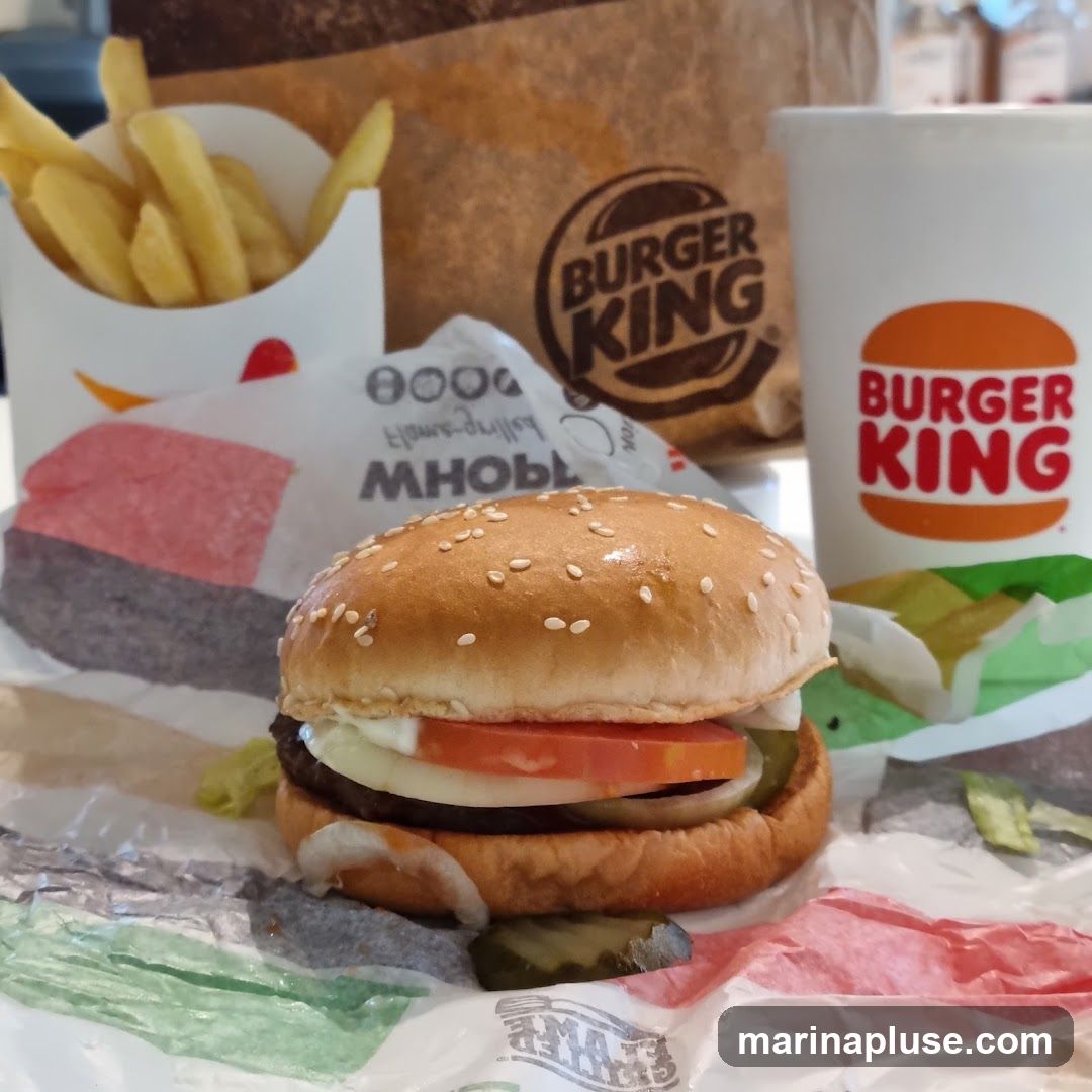 A close-up shot of a Burger King meal, featuring a Whopper burger, french fries, and a drink. The Burger King logo is visible on the cup and the paper bag in the background.